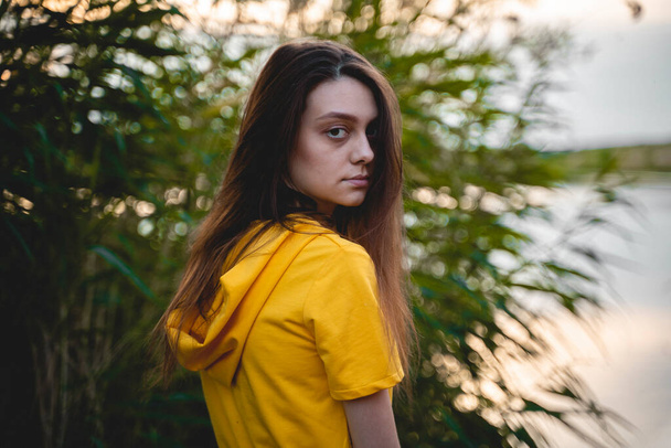A young woman in a yellow overalls stands in the river among the tall grass - Photo, Image