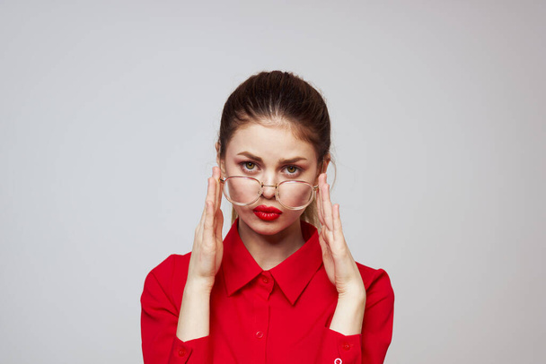 mulher na moda em uma camisa vermelha em um fundo leve emoções divertidas óculos de maquiagem brilhantes aparência atraente  - Foto, Imagem