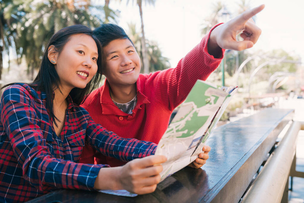 Portret szczęśliwej azjatyckiej pary podróżników trzymającej mapę i szukającej wskazówek. Koncepcja podróży i wakacji. - Zdjęcie, obraz