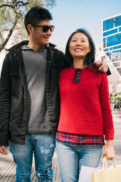 Porträt eines jungen asiatischen verliebten Paares, das nach dem Einkaufen in der Stadt spaziert. Ladenkonzept. - Foto, Bild