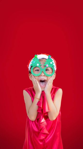 grande surpresa asiático crianças ação no vermelho vestido e árvore de Natal óculos traje no vermelho isolado fundo com vertical banner tamanho (include clipping path) - Foto, Imagem