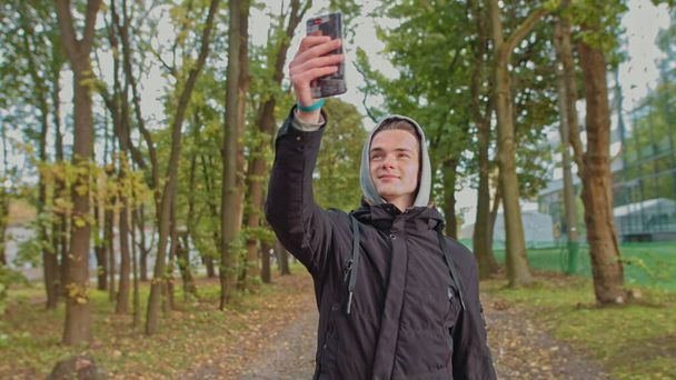 Νομοφοβία - Οι άνθρωποι που χρησιμοποιούν το κινητό τηλέφωνο. Μη-κινητή-τηλέφωνο φοβία. Ο νεαρός μιλάει σε μια βιντεοκλήση στο δρόμο στο πάρκο. Ζωή χωρίς smartphone δεν είναι δυνατή, επικοινωνία με έναν σκλάβο - Φωτογραφία, εικόνα
