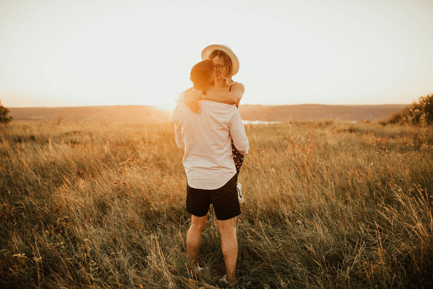 Un homme avec une femme dans un câlin chapeau et baiser dans l'herbe haute dans la prairie - Photo, image