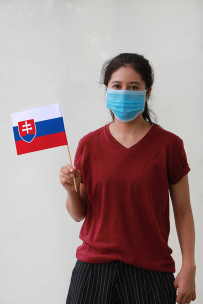 Maskierte Frau in braunem Hemd und Slowakei-Fahne in der Hand. Konzept des Schutzes und der Bekämpfung von COVID 19. - Foto, Bild