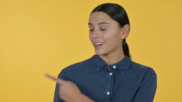 Nuori latinalaisamerikkalainen nainen osoittaa tuotetta, keltainen tausta  - Materiaali, video