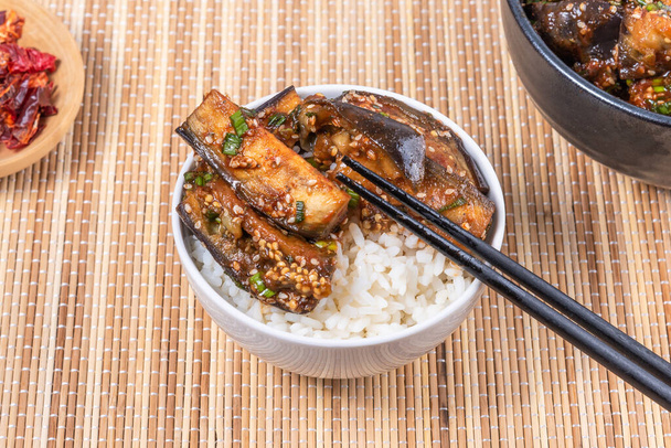 Korean style spicy eggplant with spicy sauce and sesame seeds in a bowl of rice and chopsticks on a bamboo napkin on a rustic wooden table, top view, close-up - Foto, Imagem