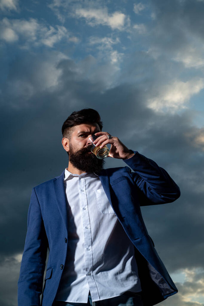 Man with beard and mustache holds alcoholic beverage on sky background. Service and alcoholism concept. - Foto, immagini