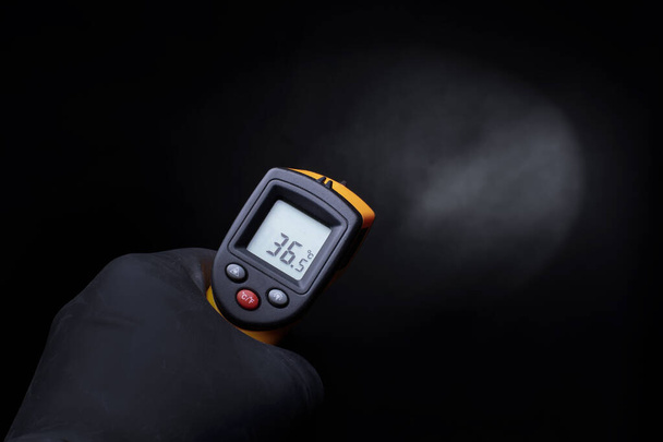 Una mano guantata tiene un termometro industriale su sfondo nero. - Foto, immagini