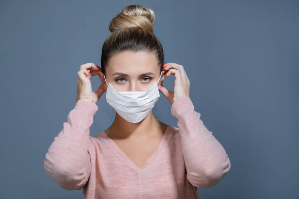 Nuori nainen laittaa lääketieteellisen naamion. Influenssan, kuumeen, pandemian, epidemian oireet. - Valokuva, kuva