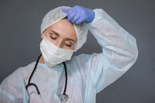 Доктор со стетоскопом, в защитной маске снимает кепку, уставшую после работы. - Фото, изображение