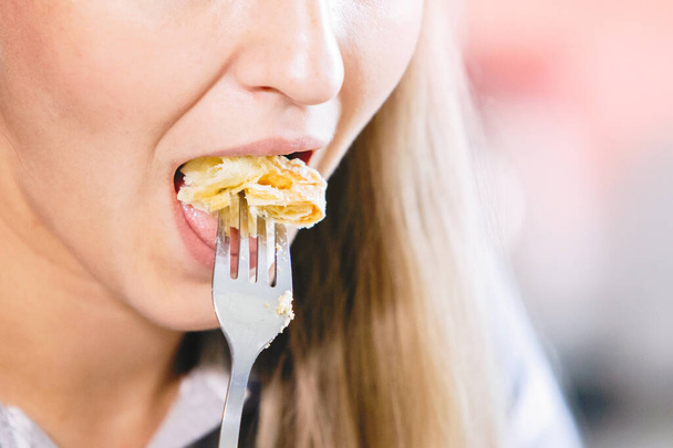 Vrouw met draadloze hoofdtelefoon eet taart met een vork. - Foto, afbeelding