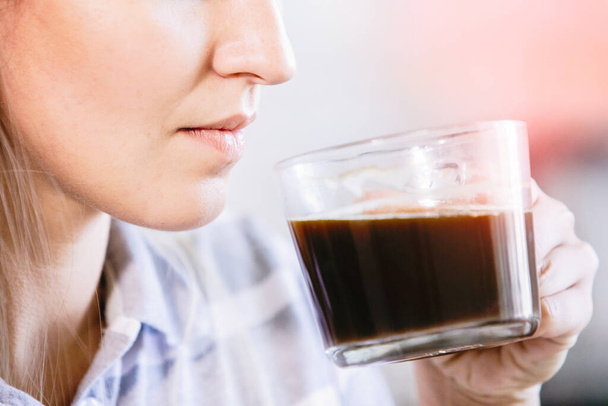 De vrouw drinkt zwarte koffie uit een doorzichtig kopje. Close-up. - Foto, afbeelding