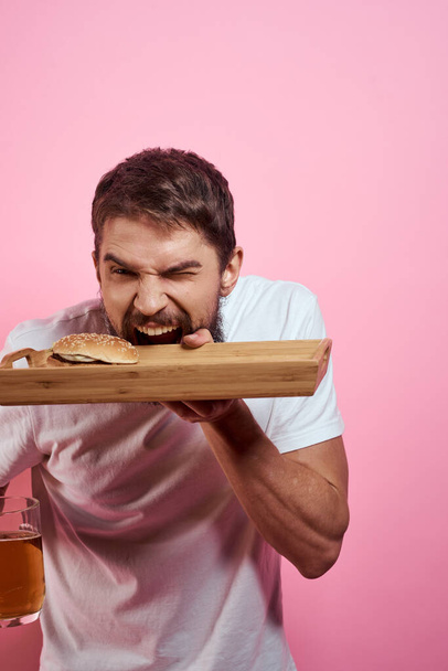 Агрессивный парень с подносом в руках гамбургер картофель фри розовый фон голодный взгляд - Фото, изображение