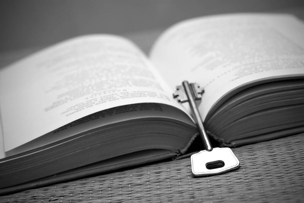 Um livro aberto e uma chave em preto e branco. Conceito de educação / sabedoria com um livro e uma chave. - Foto, Imagem
