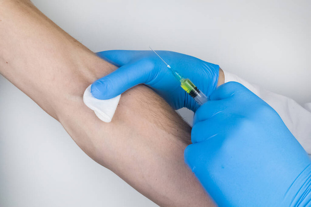 Un médecin en gants médicaux bleus fait une injection dans une veine. Administration intraveineuse de médicaments. Le concept de prestation de soins médicaux professionnels - Photo, image