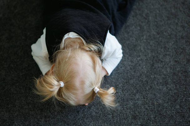 Blonde girl with ponytails lies on the floor covering her face with her hands. - Photo, Image