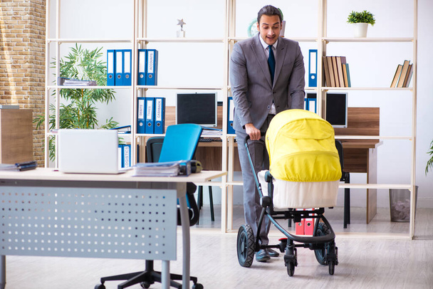 Giovane dipendente maschio che si prende cura del neonato sul posto di lavoro - Foto, immagini
