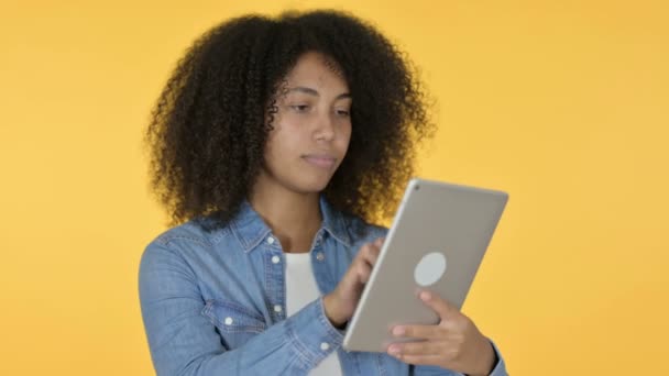 Joven mujer africana celebrando en la tableta, fondo amarillo  - Metraje, vídeo