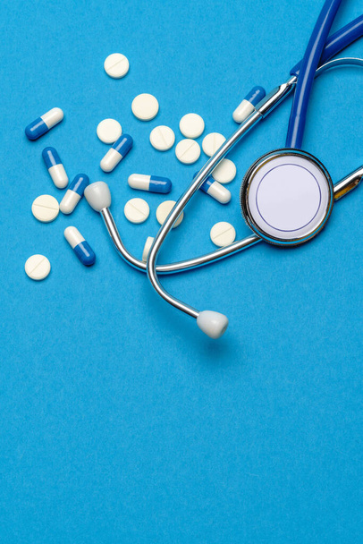 Health care or illness concept - stethoscope and pills on blue background - Foto, Imagem