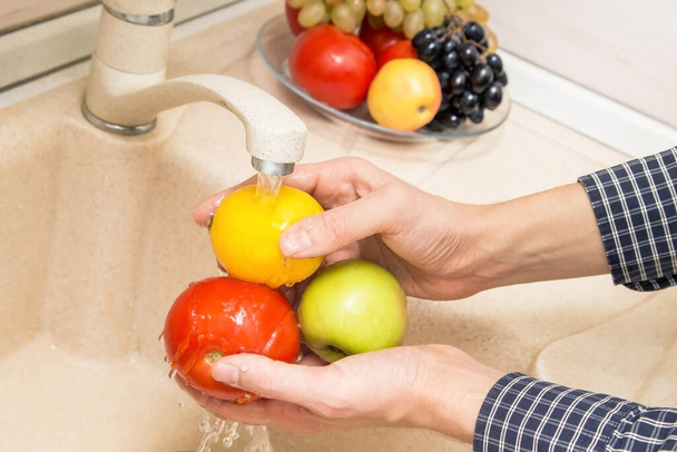 Hands washing tomato, apple and lemon in the sink on kitchen. Washing fruits and vegetables concept - Φωτογραφία, εικόνα