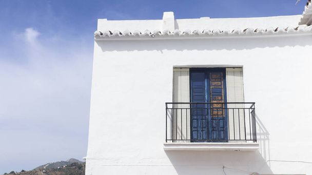 facade of a typical Andalusian house, the house is white and has a balcony with blue shutters, the upper part of the house has tiles and in the background you can see the mountains and the blue sky - Photo, Image
