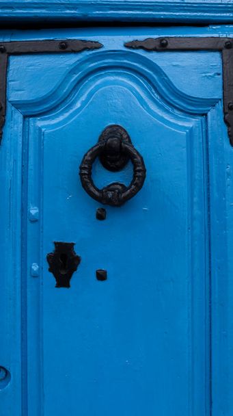 Primer plano de una puerta de madera azul con molduras, tiene un viejo golpeador en forma de círculo negro - Foto, Imagen
