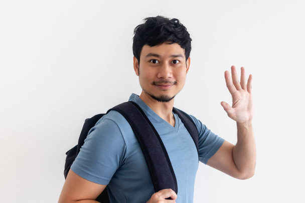 Man in blue t-shirt with backpack is waving hand on isolated background. - Foto, Imagem