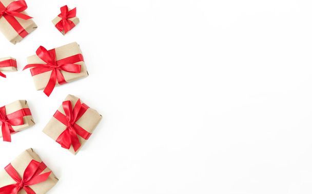 Coffrets cadeaux enveloppés dans du papier artisanal avec des rubans rouges et des arcs sur fond blanc. Pose plate festive avec espace de copie. - Photo, image