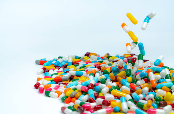 Selective focus on pile of antibiotic capsule pills. Colorful antibiotic capsules pill falling on white table. Antibiotic drug resistance concept. Antimicrobial drug overuse. Pharmaceutical industry. - Photo, Image