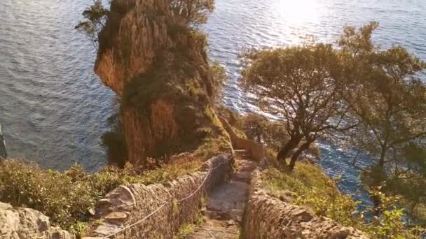 Magischer Blick auf das Meer bei Sonnenaufgang von einem gepflasterten Treppenweg inmitten einer Klippe mit Pflanzen ringsum - Filmmaterial, Video