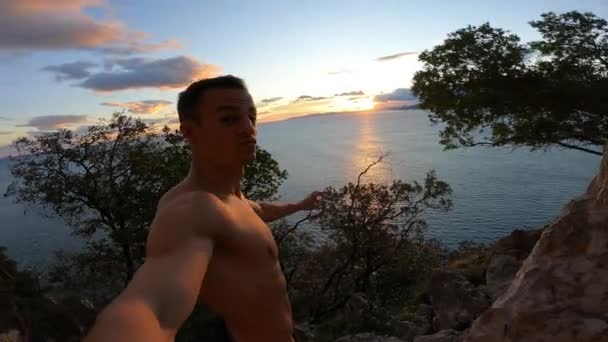 Lihaksikas nuori kaveri paidaton nauttia auringonnoususta kalliolta merelle päin - Materiaali, video