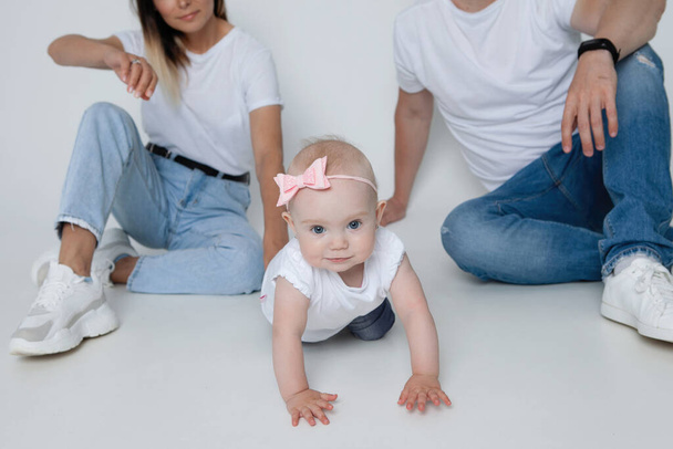Glückliche Familie - Mama, Papa und Baby im Studio. Lässige Kleidung weiße T-Shirts, blaue Jeans. Glückliche Kindheit, elterliche Fürsorge, schönes Mädchen. - Foto, Bild
