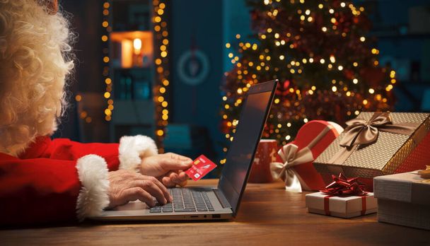 Santa doing online shopping at Christmas, he is connecting online with his laptop and paying with his credit card - Valokuva, kuva