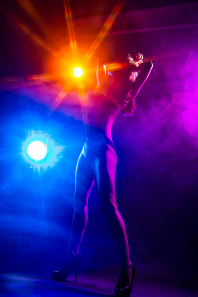 Beautiful slim sexy dancer girl wearing lingerie and high heels posing in the rays of light in a colorful smoke. Artistic, conceptual, silhouette,commercial and advertising design. - Photo, image