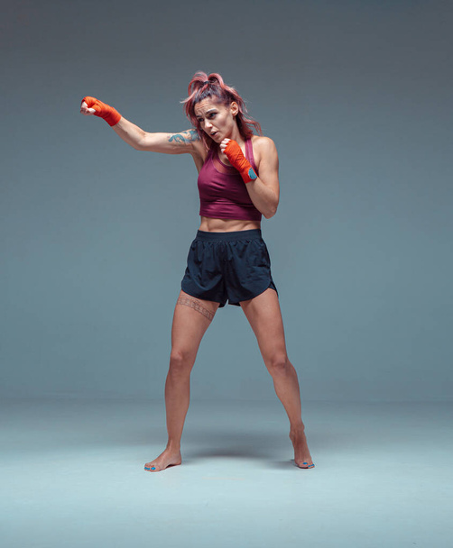 Female fighter trains in boxing bandages in studio on gray background. - Foto, immagini