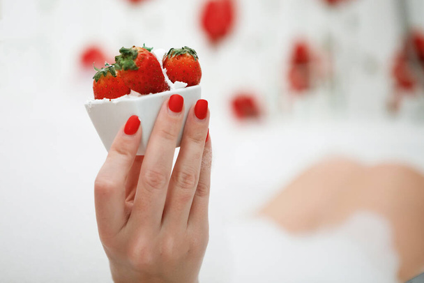 Female hand with a red manicure holds a vase with strawberries. Selected Focus. - Foto, immagini