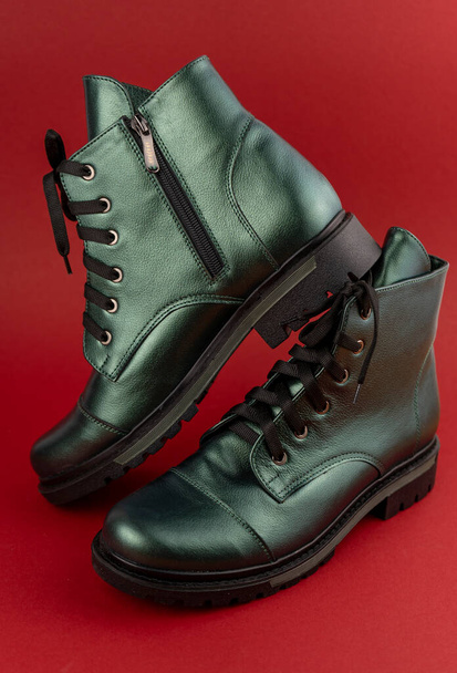 Green leather shoes. Winter and autumn off-season boots. Stylish boot isolated on red background. Close-up. Laces, tractor sole, comfortable last. Casual style. Copy space. Pearlescent color. - 写真・画像