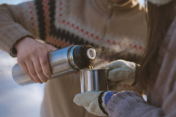 Ein Mann gießt einer Frau ein Heißgetränk aus einer Thermoskanne in eine Tasse. Winterspaziergang. Nahaufnahme. - Foto, Bild