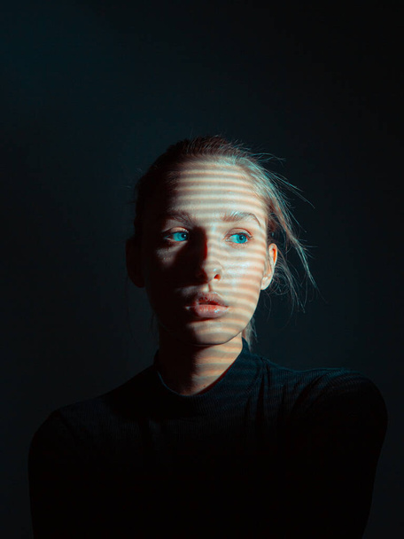 Mysterious portrait of girl with shadow pattern on her face in dark black studio - Photo, image