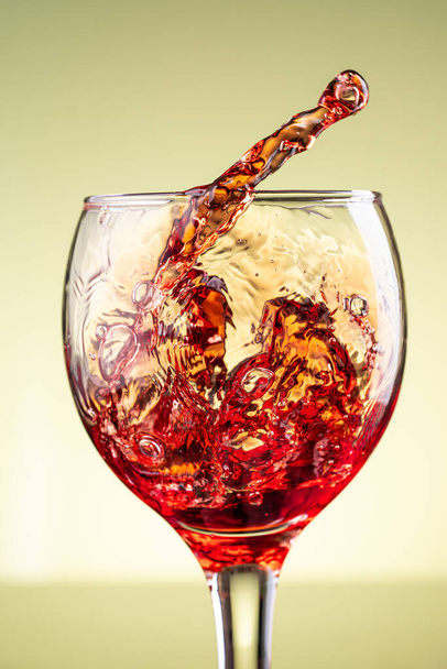 splash of red wine in glass on yellow background - Photo, Image