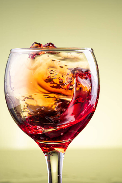 splash of red wine in glass on yellow background - Photo, Image