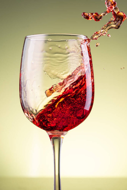 splash of red wine in glass on yellow background - Foto, afbeelding