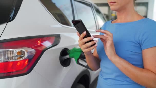 Žena pomocí chytrého telefonu, zatímco její auto tankování - Záběry, video