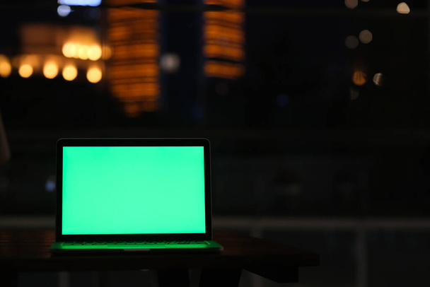 visão frontal do computador portátil tela verde na noite escura. Desfocado cidade luzes fundo - Foto, Imagem