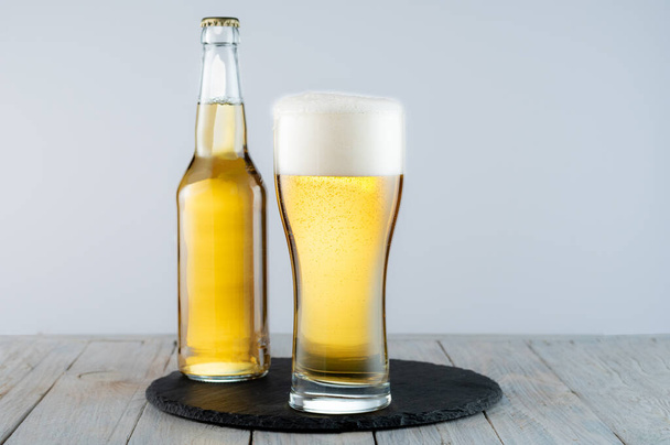 A glass of light beer on a tray. Bottle and glass of light beer. Beer on the table. - Photo, image