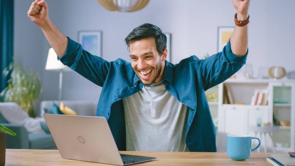 Happy Handsome Man Working on a Laptop Celebrates Successful Endeavor with YES Gesture. Freelances Working from His Living Room Has Stroke of Luck and Wins Big. - Fotoğraf, Görsel