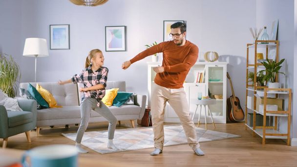 Happy Little Girl Dances with Young Father in the Middle of the Living Room. Happy Family Time, Father and Daughter Dancing at Home. - Photo, image