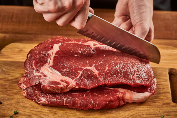 Chef cutting beef meat with Santoku knife on wooden cutting board - Fotó, kép