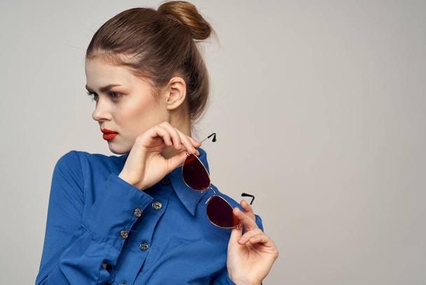 Donna alla moda in occhiali da sole e una camicia blu gesticolando con le mani su uno sfondo chiaro vista ritagliata - Foto, immagini