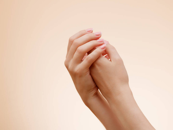 Imagen de cerca de las manos de una hermosa mujer con manicura francesa rosa claro en las uñas. Cuidado de la piel para las manos, manicura y tratamiento de belleza. Manos elegantes y elegantes con dedos finos y elegantes. - Foto, Imagen